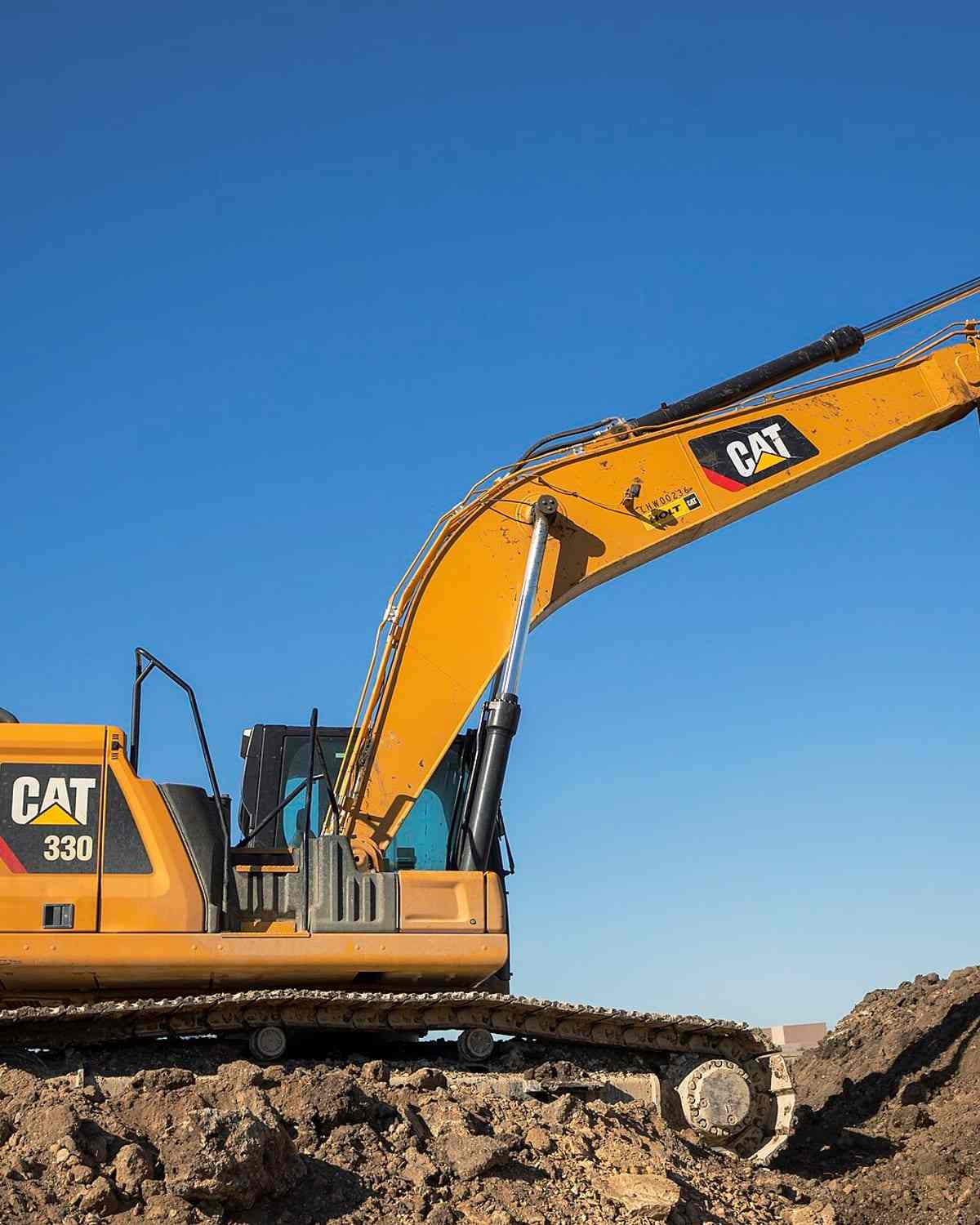 A tracked excavator standing on a stripped earthworks platform against an open sky